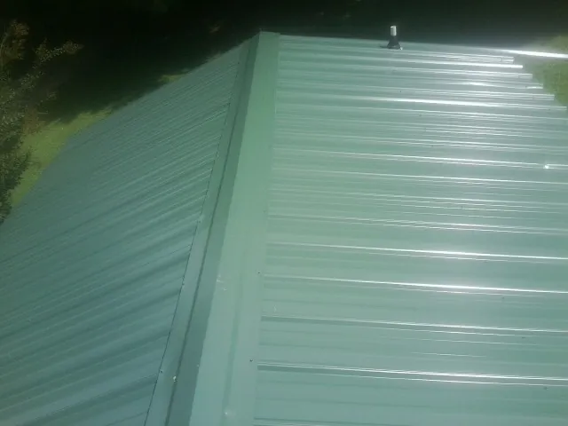 New green metal panels meeting at the ridge of a roof — Flat Roof Repair work by our crew in Adamsville