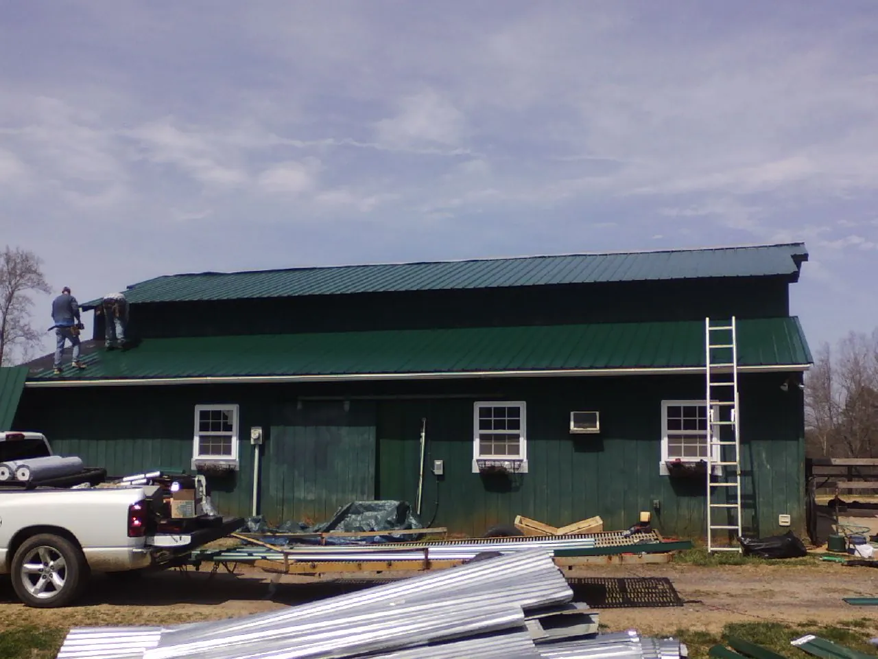 Crew installing green metal roofing on a large green barn in Adamsville