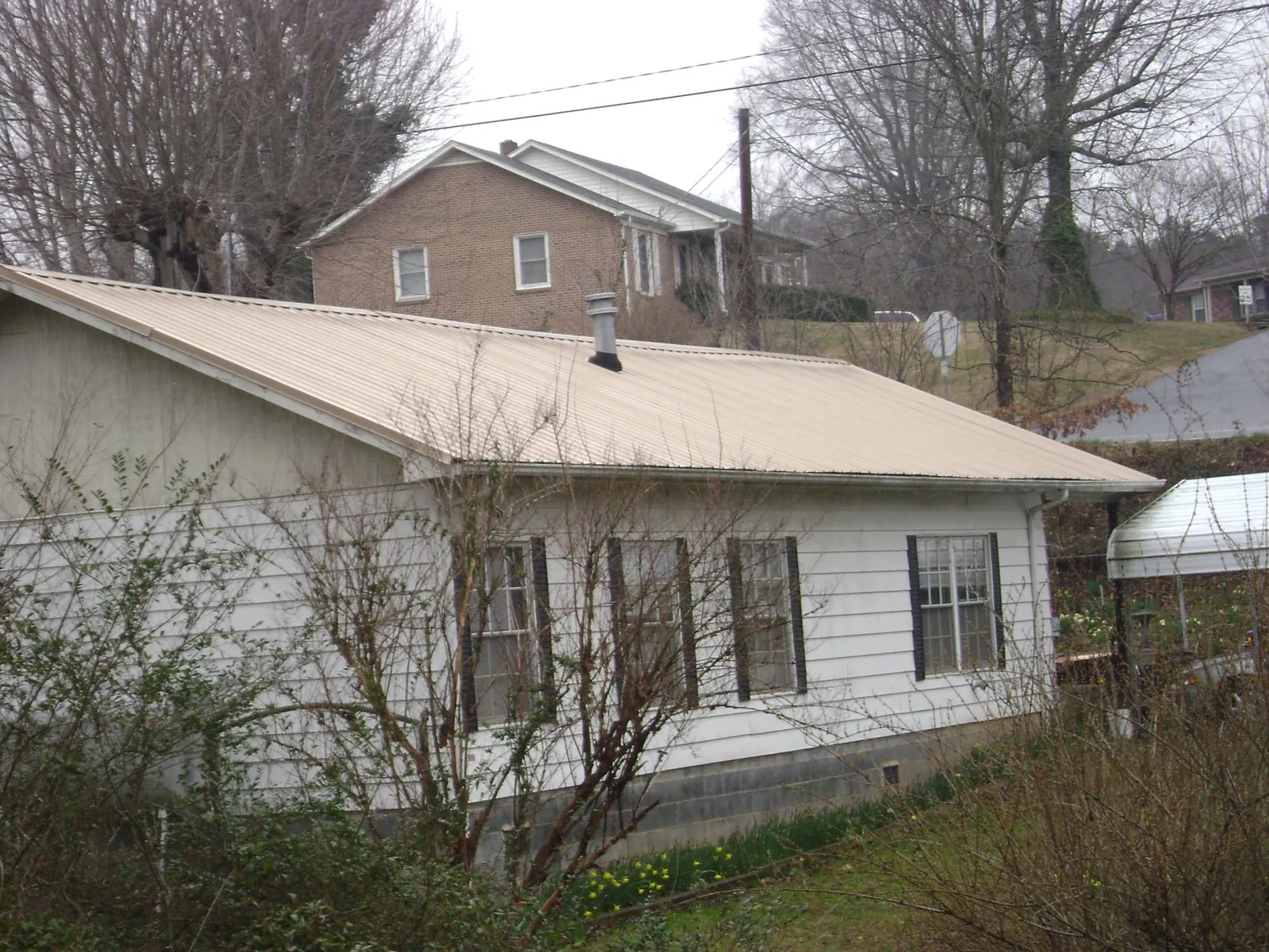 Tan metal roof on a white sided house set into a hillside — Commercial Roofing by Roofing Brothers in Adamsville